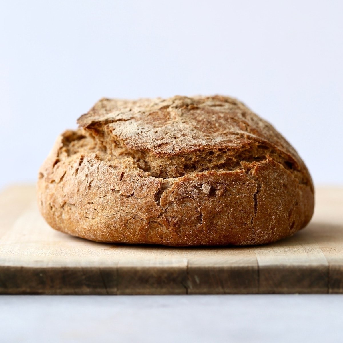 Crusty, golden brown whole wheat artisan bread on a wooden cutting board.