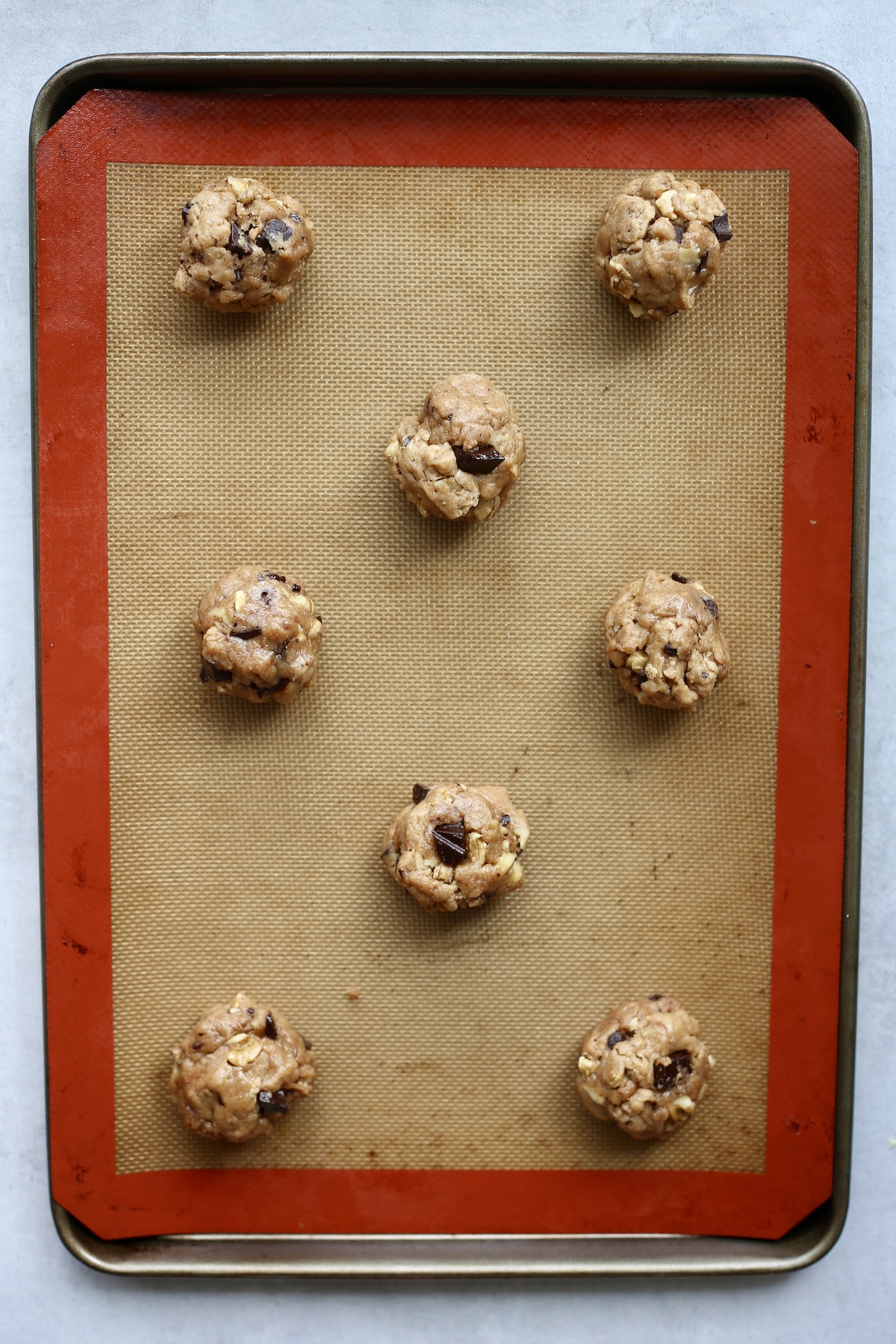 Raw whole wheat chocolate chip cookie dough portioned into balls and spread out on a baking sheet. 