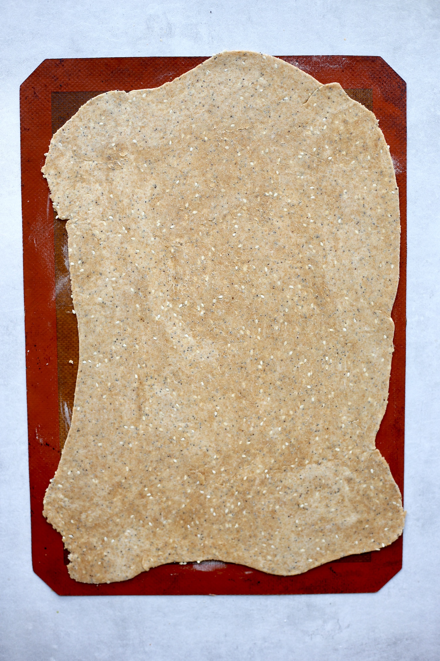 Whole wheat sesame cracker dough rolled out into a thin rectangle on a silicone baking mat. 