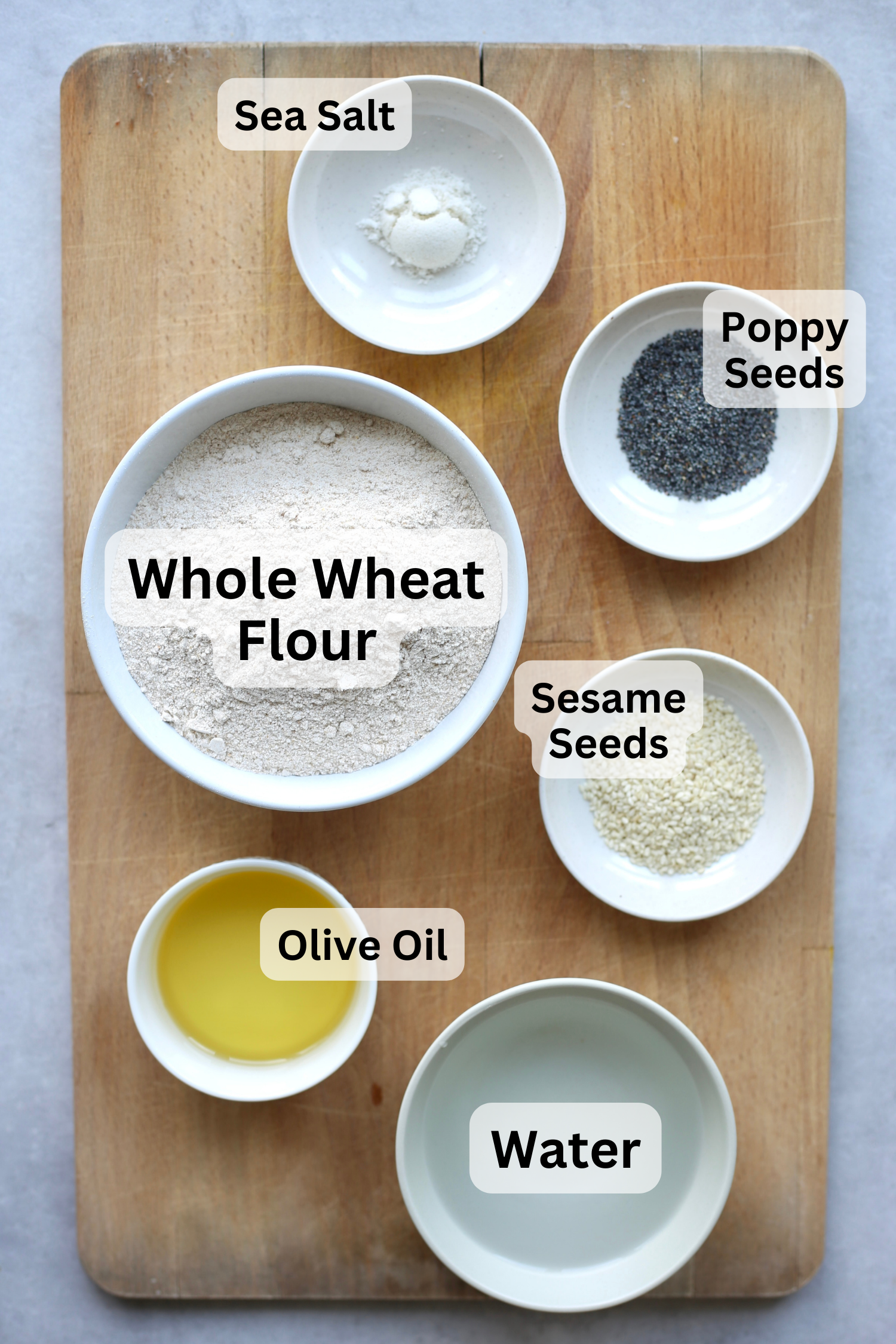 All of the ingredients for whole wheat crackers measured out into bowls and laid out on a wooden cutting board. 