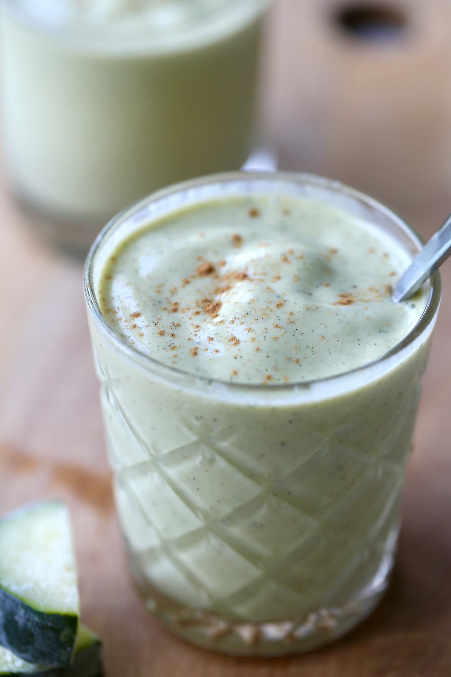 A creamy, light green colored zucchini smoothie topped with a sprinkling of cinnamon.