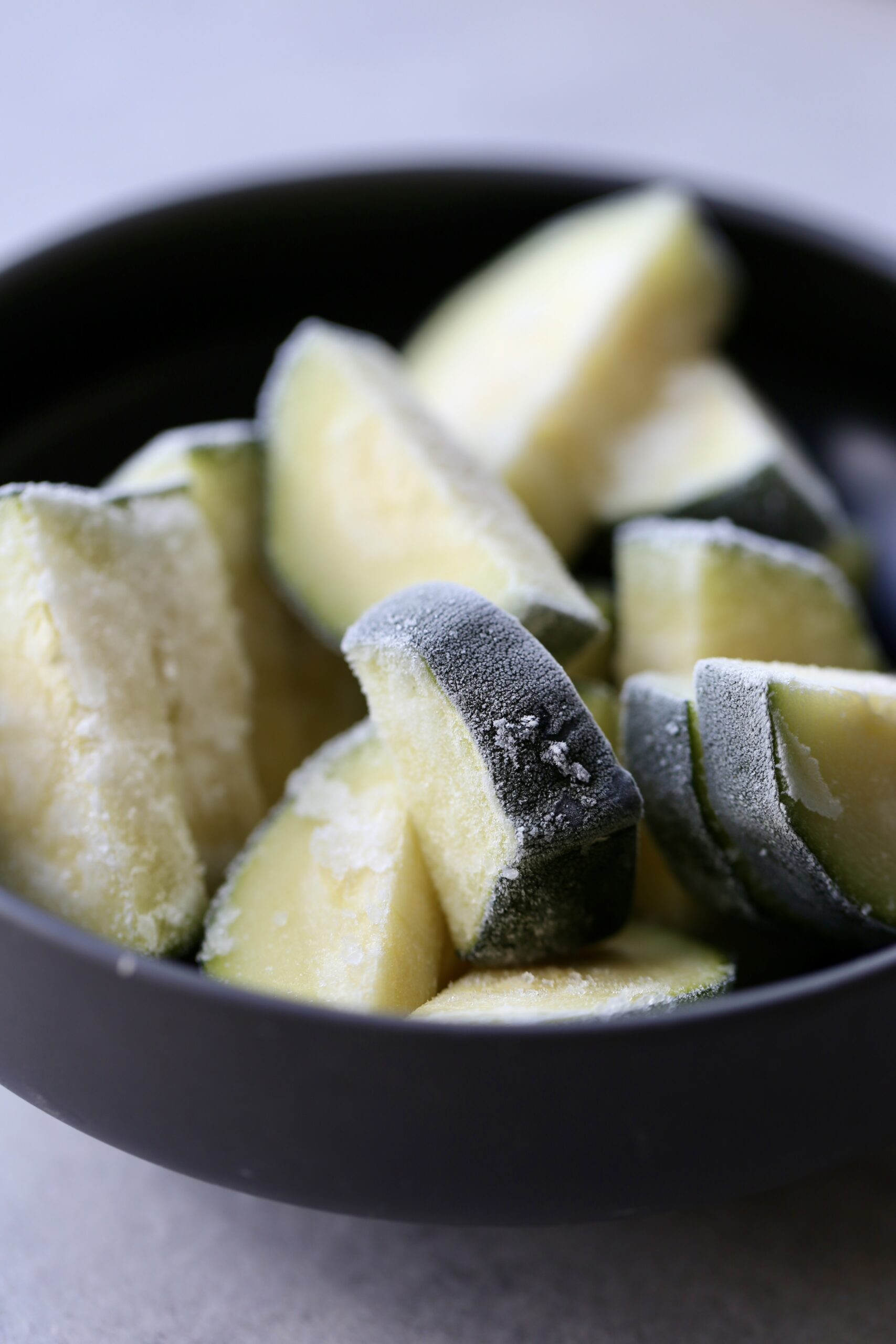 Chopped frozen zucchini in a black bowl. 