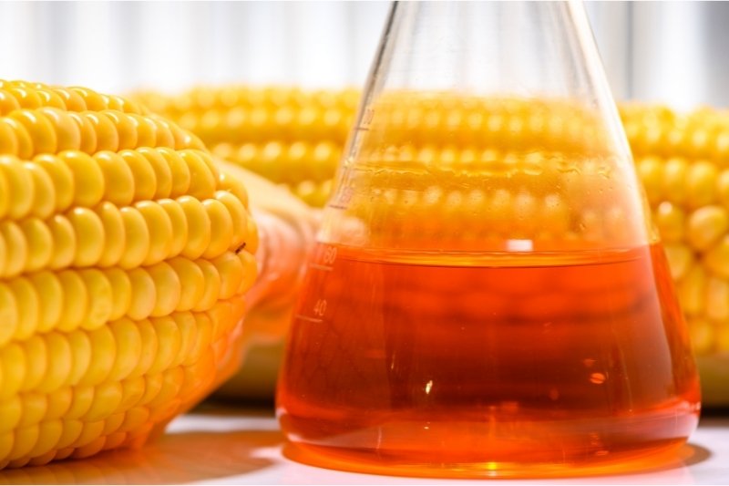 two ears of corn next to a chemical lab flask of corn syrup