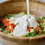 vegan Caesar salad dressing being poured over a bowl of greens