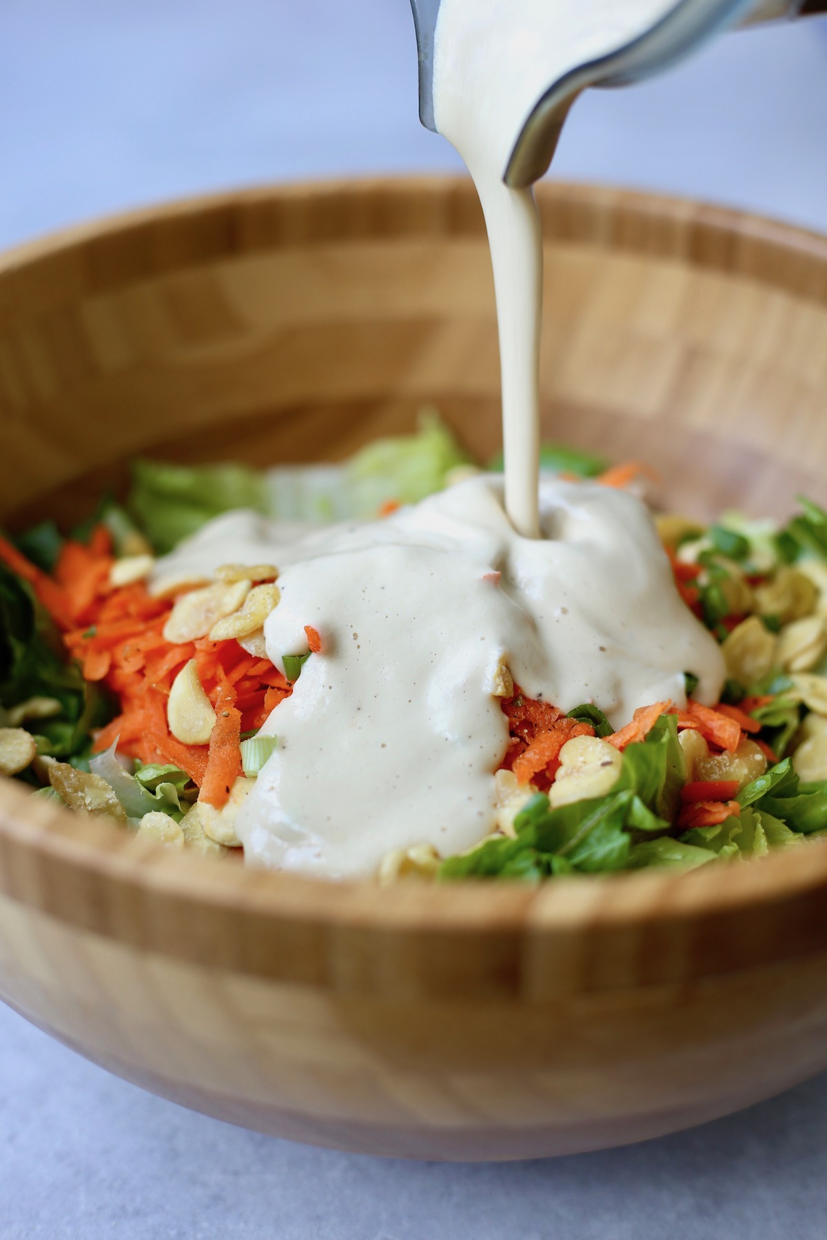 homemade vegan Caesar dressing being poured over a large bowl of greens