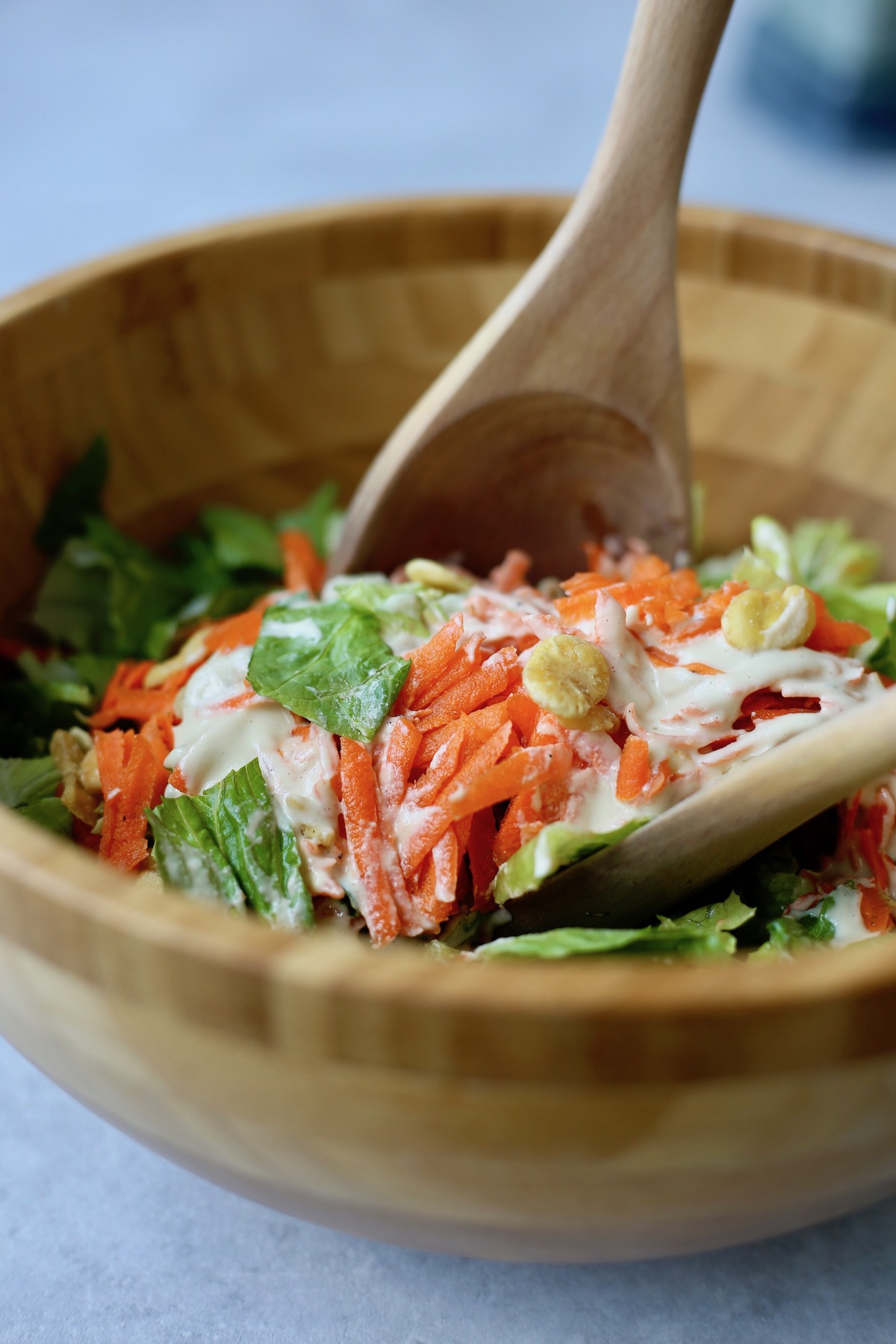 shredded carrots, romaine and vegan Caesar dressing being mixed together in a bowl